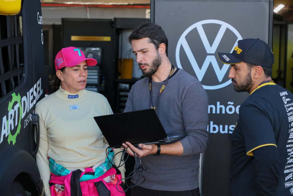 Equipe técnica analisando pneus de corrida ao lado de um carro de corrida.