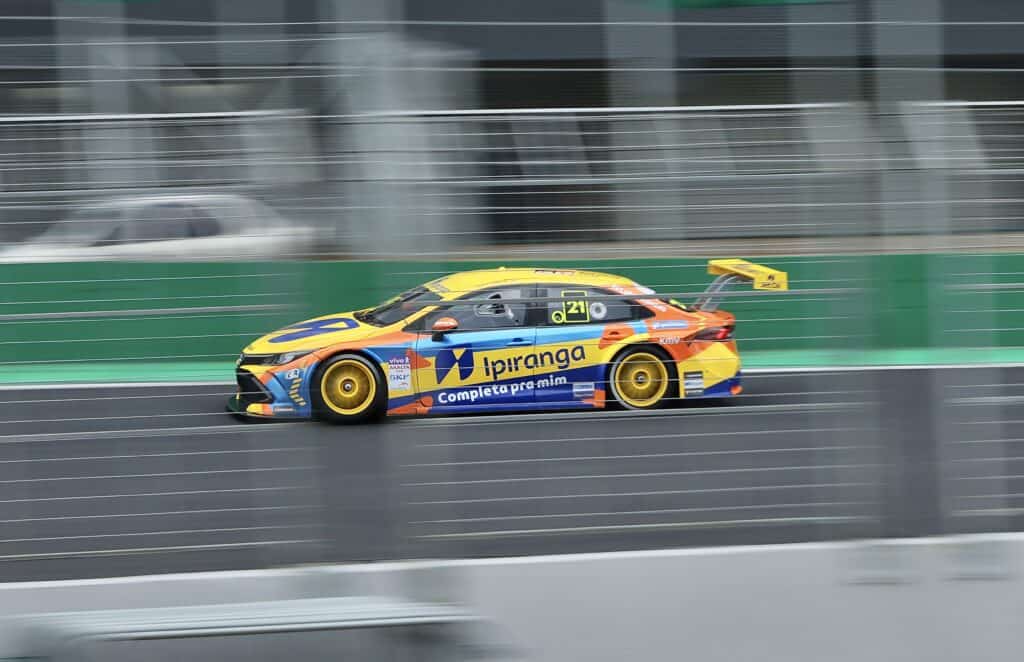 Porsche de corrida com cores amarelas, azuis e laranja em alta velocidade na pista.