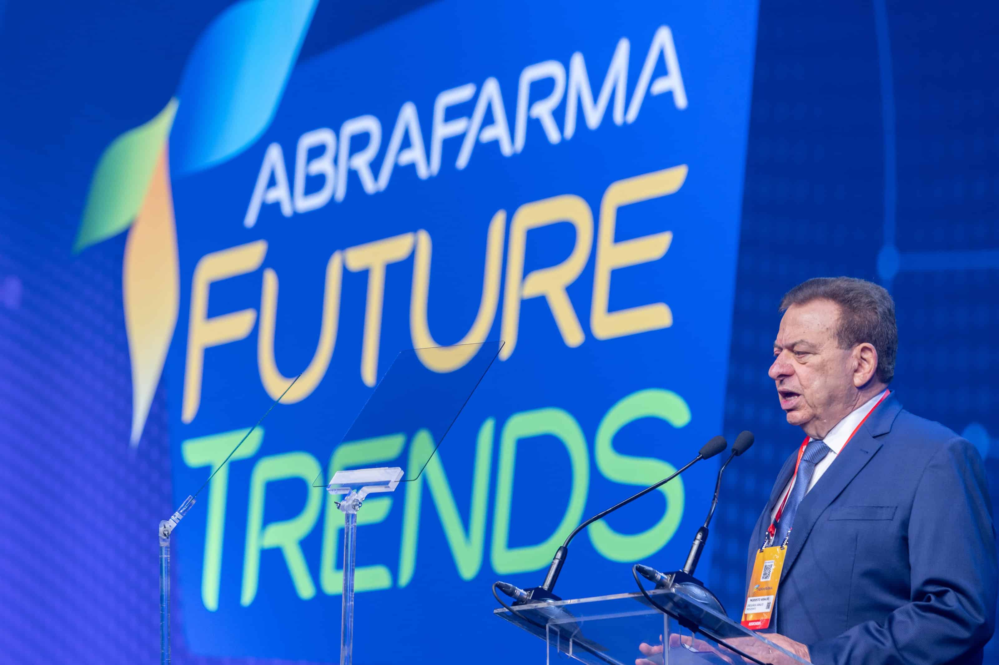 Imagem de um palestrante em conferência na ABRAFARMA Future Trends, com tela ao fundo exibindo o log.