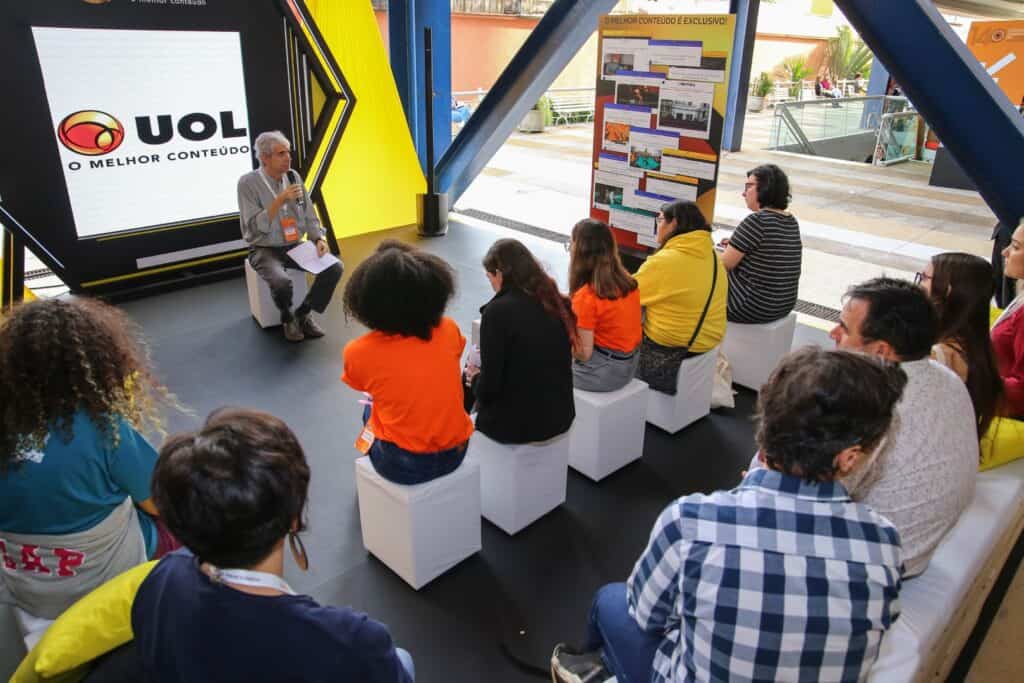 Imagem de uma palestra com público assistindo atentamente em ambiente interno moderno.